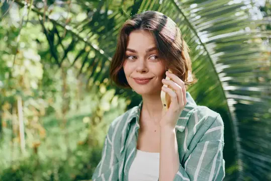 Молодая женщина с телефоном у пальмовых листьев