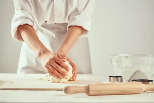 Женщина в фартуке месит тесто на кухонном столе