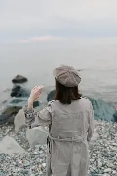 Женщина в берете и плаще машет рукой у моря