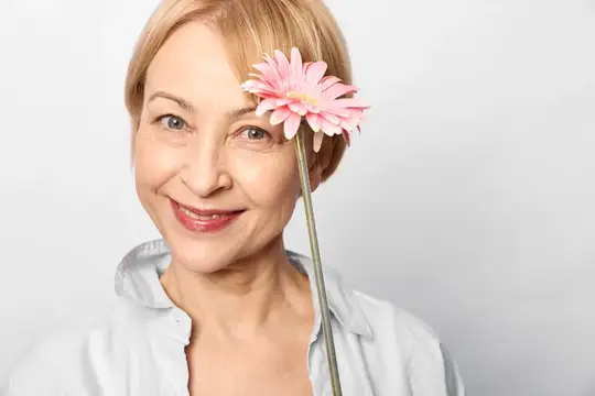 Улыбающаяся светловолосая женщина с розовой герберой у лица