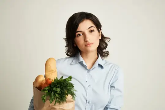 Милой брюнетке доставляют продуктовый пакет из супермаркета на светлом фоне
