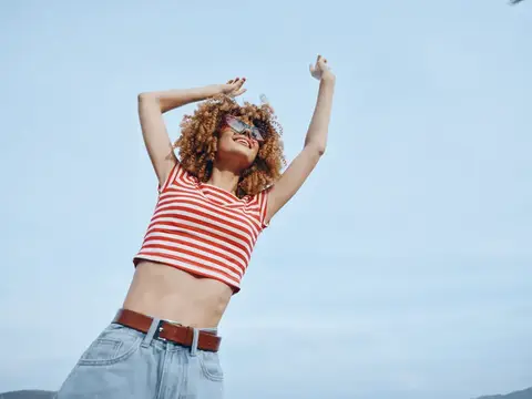 Рыжеволосая девушка в солнечных очках радуется на фоне неба