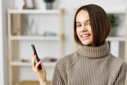 Улыбающаяся девушка с телефоном в руке дома