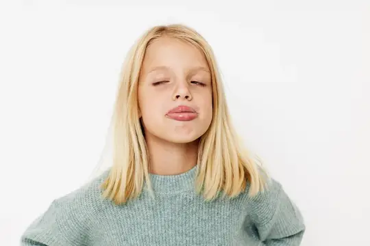 Эмоциональная девочка с blond волосами позирует в студии