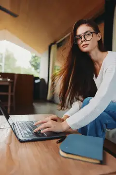 Улыбающаяся женщина-учитель работает из дома, сидя на диване и пользуясь ноутбуком в уютной гостиной