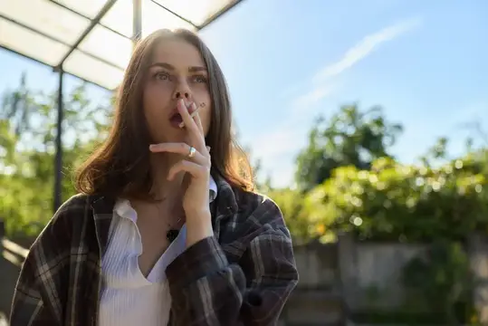 Молодая женщина с сигаретой в задумчивости смотрит вдаль на улице
