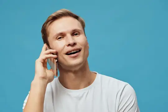 Улыбающийся светловолосый мужчина говорит по телефону на голубом фоне
