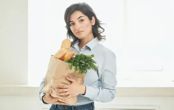 Брюнетка с пакетом продуктов: овощей, зелени — совершает покупки в супермаркете