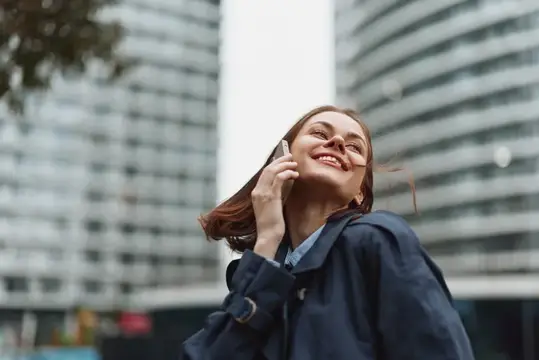Улыбающаяся шатенка говорит по телефону на фоне высоток