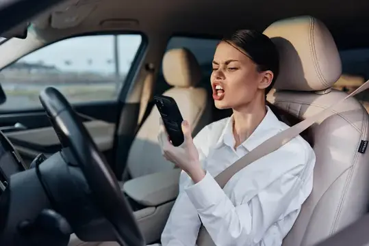 Женщина-водитель в автомобиле разговаривает по мобильному телефону с открытым ртом, прижав трубку к уху