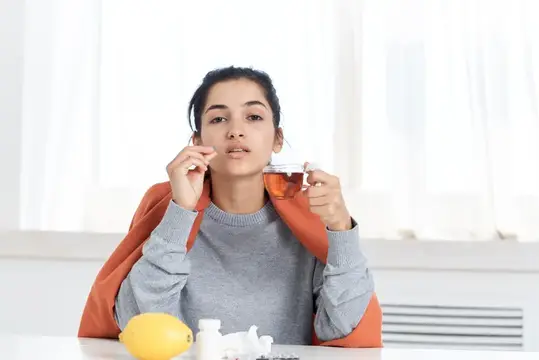 Молодая женщина пьёт чай с лимоном и лекарствами