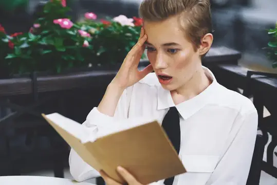 Удивлённая девушка с короткой стрижкой читает книгу за столиком кафе