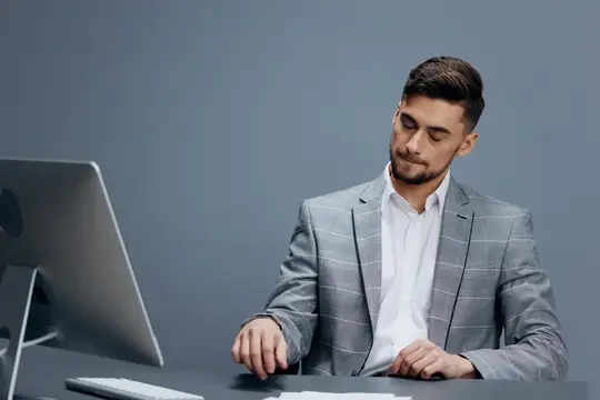 Молодой мужчина в сером пиджаке работает за компьютером в офисе