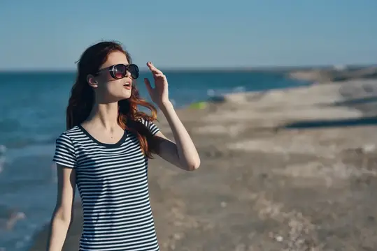 Портрет женщины в футболке и очках на пляже в горах у моря