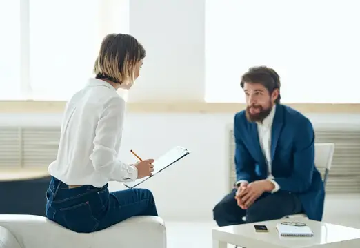 Женщина с блокнотом беседует с бородатым мужчиной в офисе