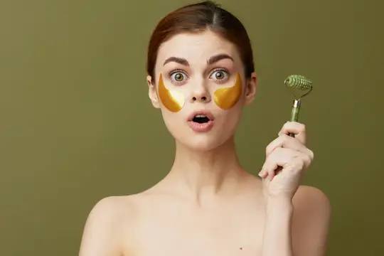 Удивлённая девушка с золотыми патчами и массажным роллером