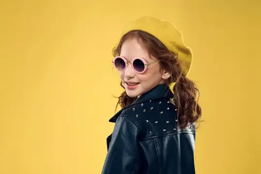 Девочка в желтой шляпе и темных очках, одетая в модную одежду, ведет активный образ жизни в студии
