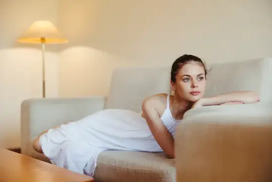 Счастливая девушка улыбается, лежа на диване дома, отдыхает в домашней обстановке, уют, солнечный свет