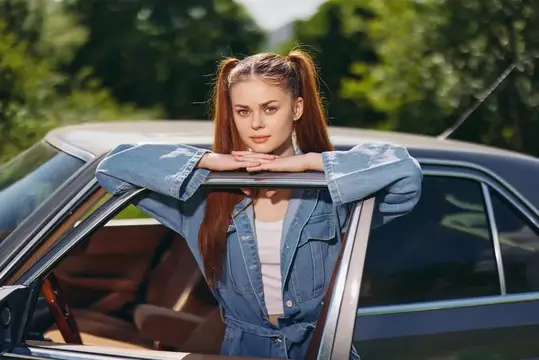 Рыжеволосая девушка с хвостиками облокотилась на крышу автомобиля