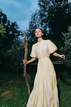 Девушка в жёлтом платье с деревянной палкой в саду
