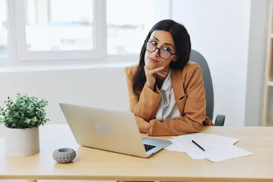 Деловая женщина работает в офисе за своим столом с ноутбуком, одетая в бежевый костюм и белую рубашку, в очках, проводит онлайн-видеочат, учительница занимается со студентами