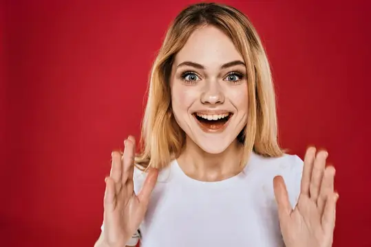 Светловолосая девушка радостно улыбается и жестикулирует на красном фоне