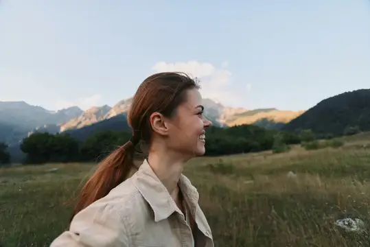 Улыбающаяся девушка с хвостом на фоне гор и луга