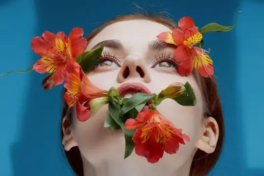 Молодая женщина с красными цветами у лица на синем фоне