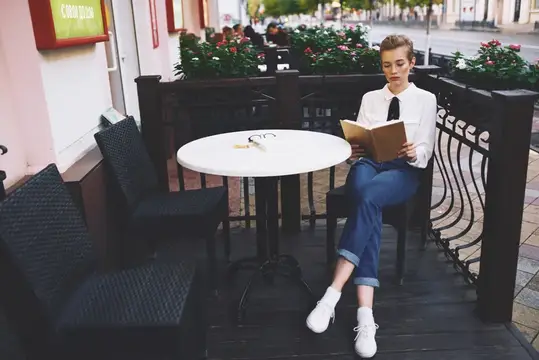 Женщина читает книгу за столиком в кафе