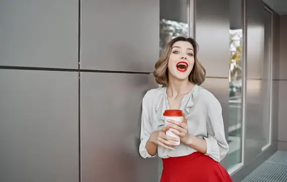 Улыбающаяся женщина с кофе у серой стены здания