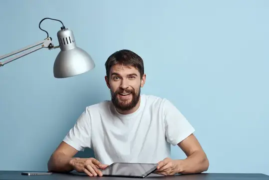 Мужчина с планшетом за столом в помещении, лампа, работа, офис, фрилансер на синем фоне