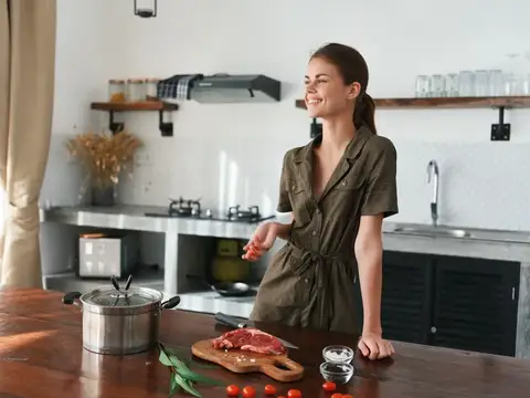Женщина улыбается на кухне, готовит обед из мяса, овощей и специй на деревянном столе на фоне стильной кухни