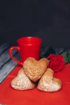 Сердечки из песочного теста с красной кружкой и розой на красном фоне