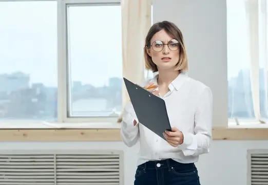 Молодая женщина в очках с папкой у окна офиса