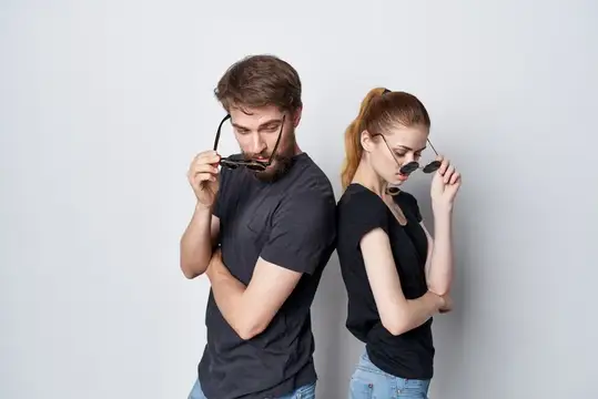 Мужчина и женщина в чёрных футболках стоят спиной к спине и снимают очки
