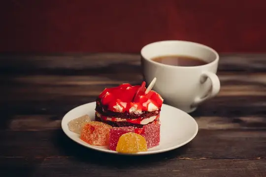 Кусочек торта с мармеладом и чашка кофе на деревянном столе