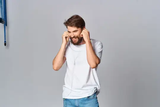 Бородатый мужчина в белой футболке слушает музыку в наушниках