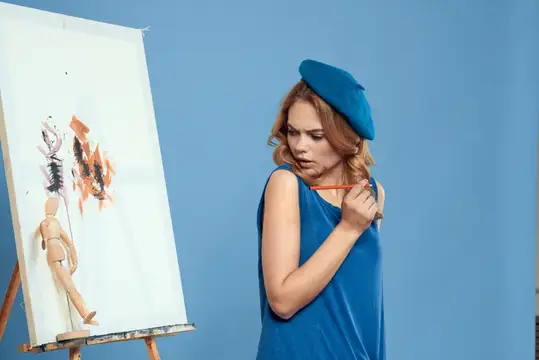 Женщина-художница с кистью рисует красками на холсте, стоящем на мольберте