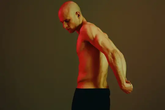 Лысый мужчина с рельефными мышцами позирует в профиль на тёмном фоне