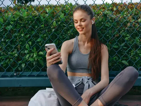 Девушка в спортивной форме сидит со смартфоном у сетки