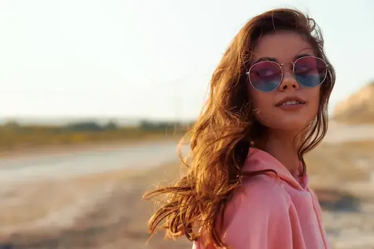 Молодая женщина в розовом худи и круглых очках на закате