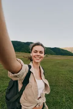 Улыбающаяся девушка с рюкзаком делает селфи на фоне зелёных гор