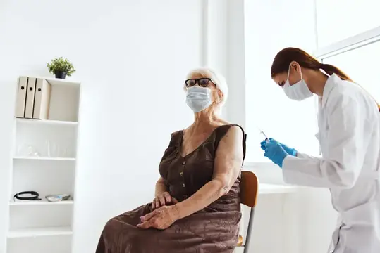 Пожилая женщина с врачом, держащим шприц с вакциной против вирусной эпидемии