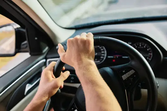Мужские руки уверенно держат руль автомобиля в салоне