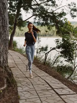 Молодая женщина бежит по каменной дорожке вдоль озера