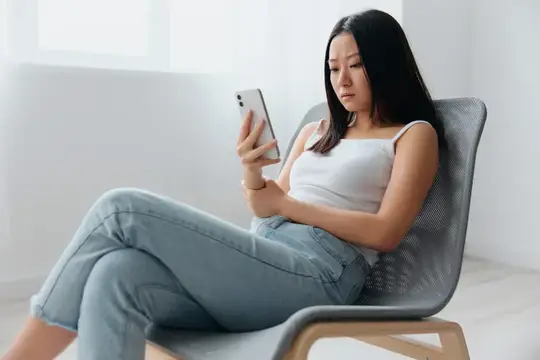 Азиатская девушка сидит в кресле и смотрит в телефон