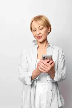 Пожилая женщина держит смартфон, расслабленная улыбка во время набора текста на экране