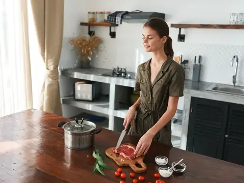 Молодая женщина нарезает мясо на кухонной доске