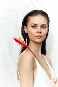 Молодая женщина с тропическим цветком у плеча на светлом фоне
