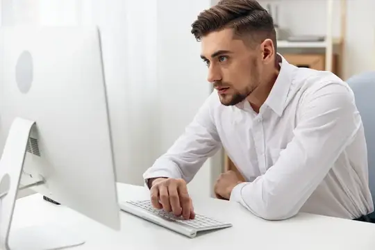 Сосредоточенный мужчина в белой рубашке работает за компьютером